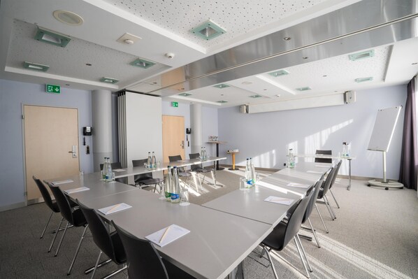 Un salón de conferencias con una larga mesa, sillas, una pizarra y un proyector.