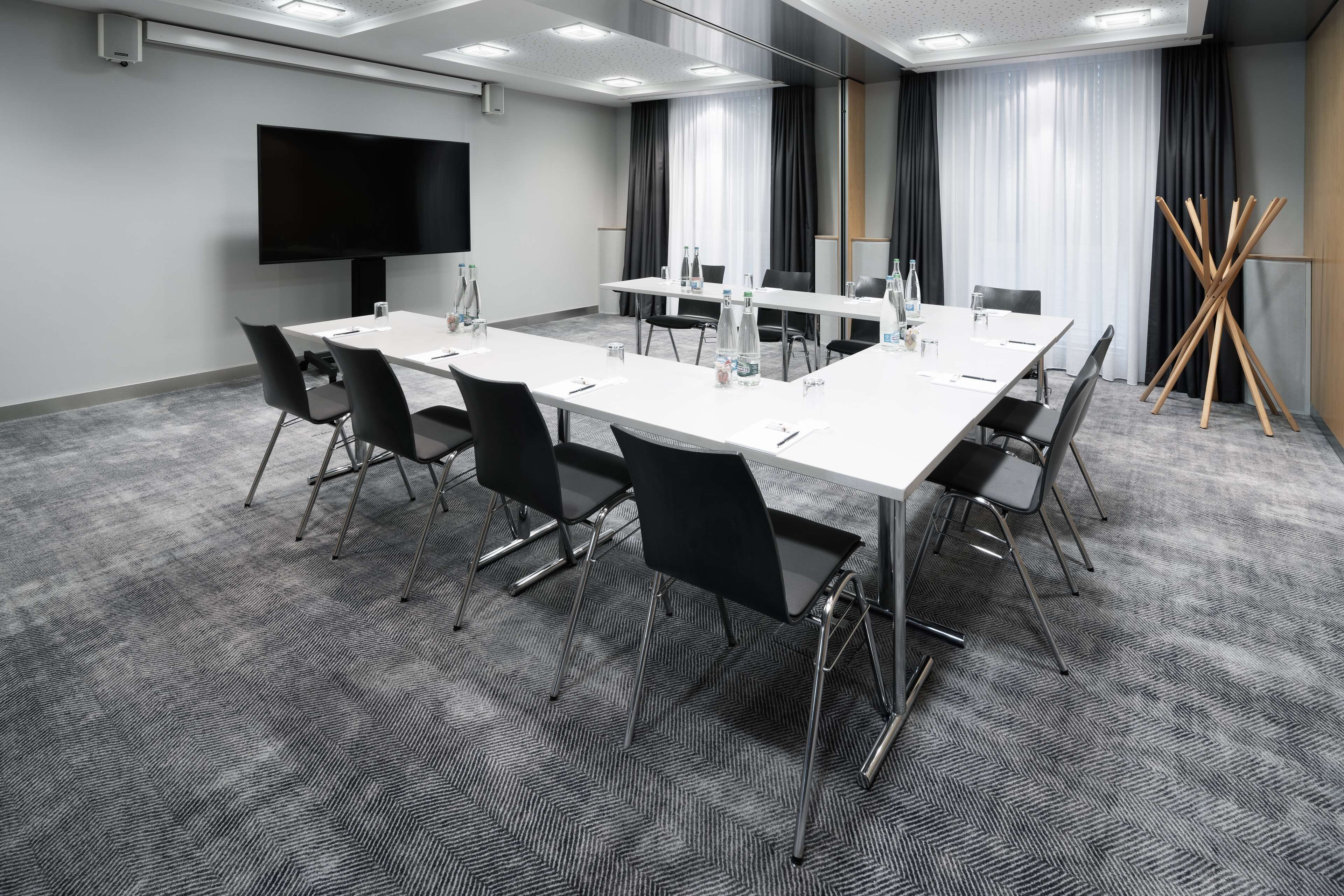 A conference room with a long table, black chairs, a flat-screen TV, and a large window with curtains.