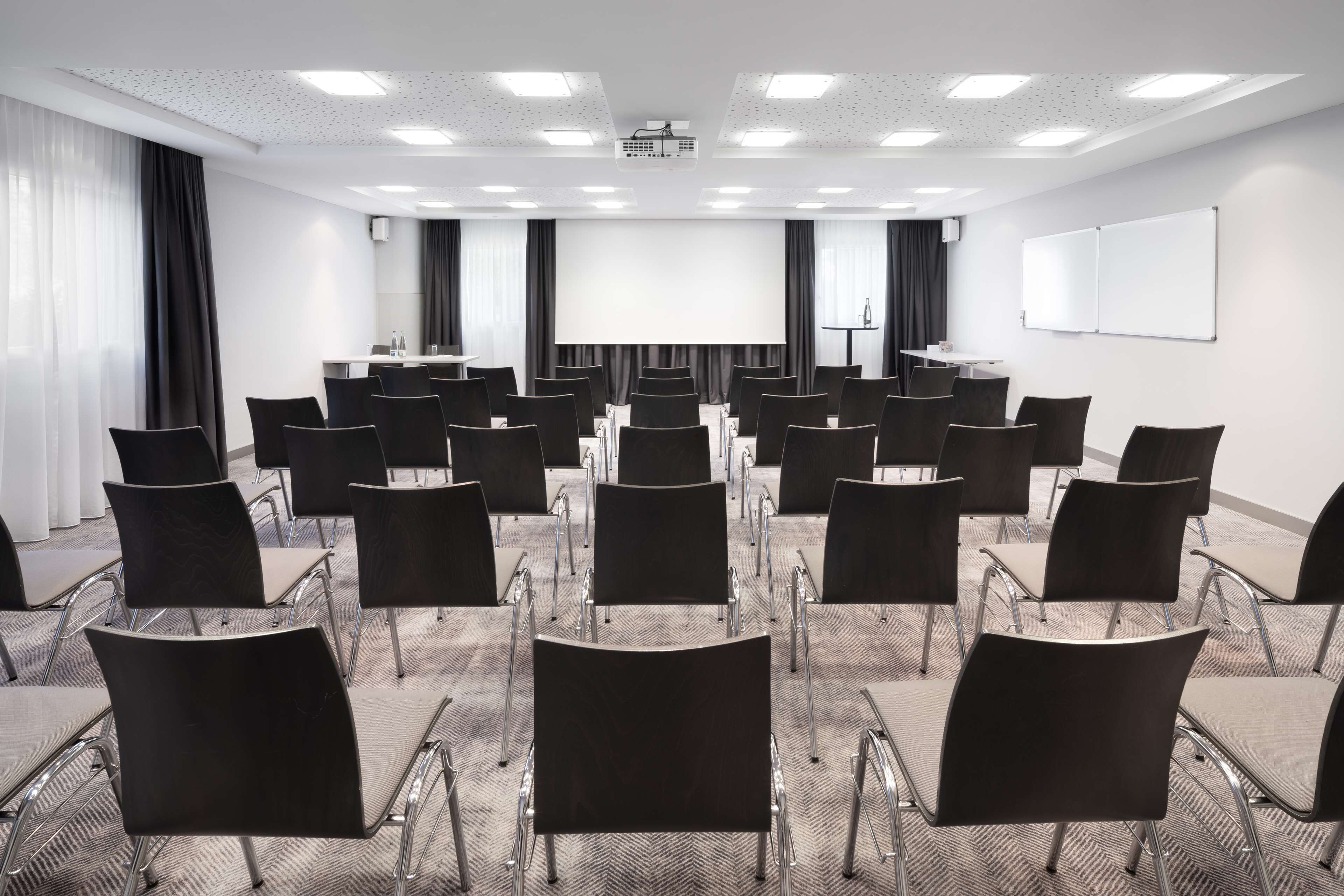 A conference room with rows of chairs, a large screen, and a projector.