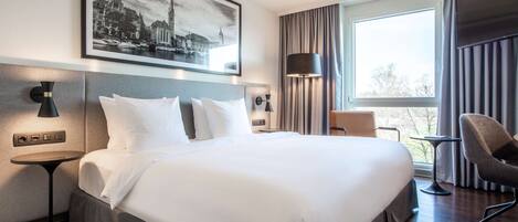 A hotel room with a large bed, a desk, a chair, a TV, and a window with curtains.