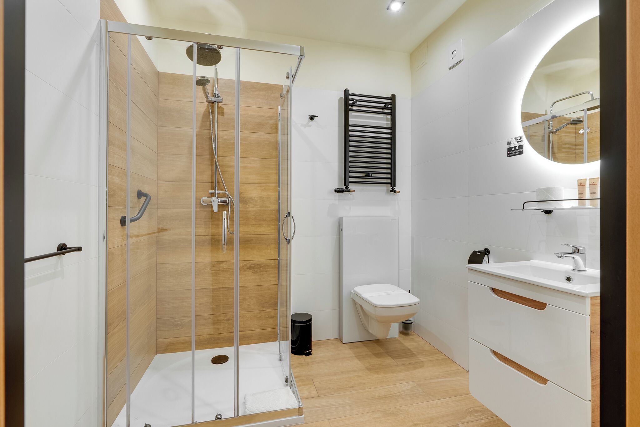 A modern bathroom with a glass-enclosed shower, a white toilet, and a sink with a mirror above it.