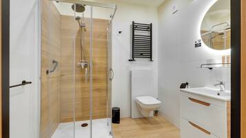 A modern bathroom with a glass-enclosed shower, a white toilet, and a sink with a mirror above it.