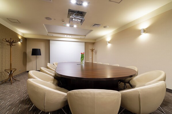 A conference room with a round table, beige chairs, a projector, and a screen.