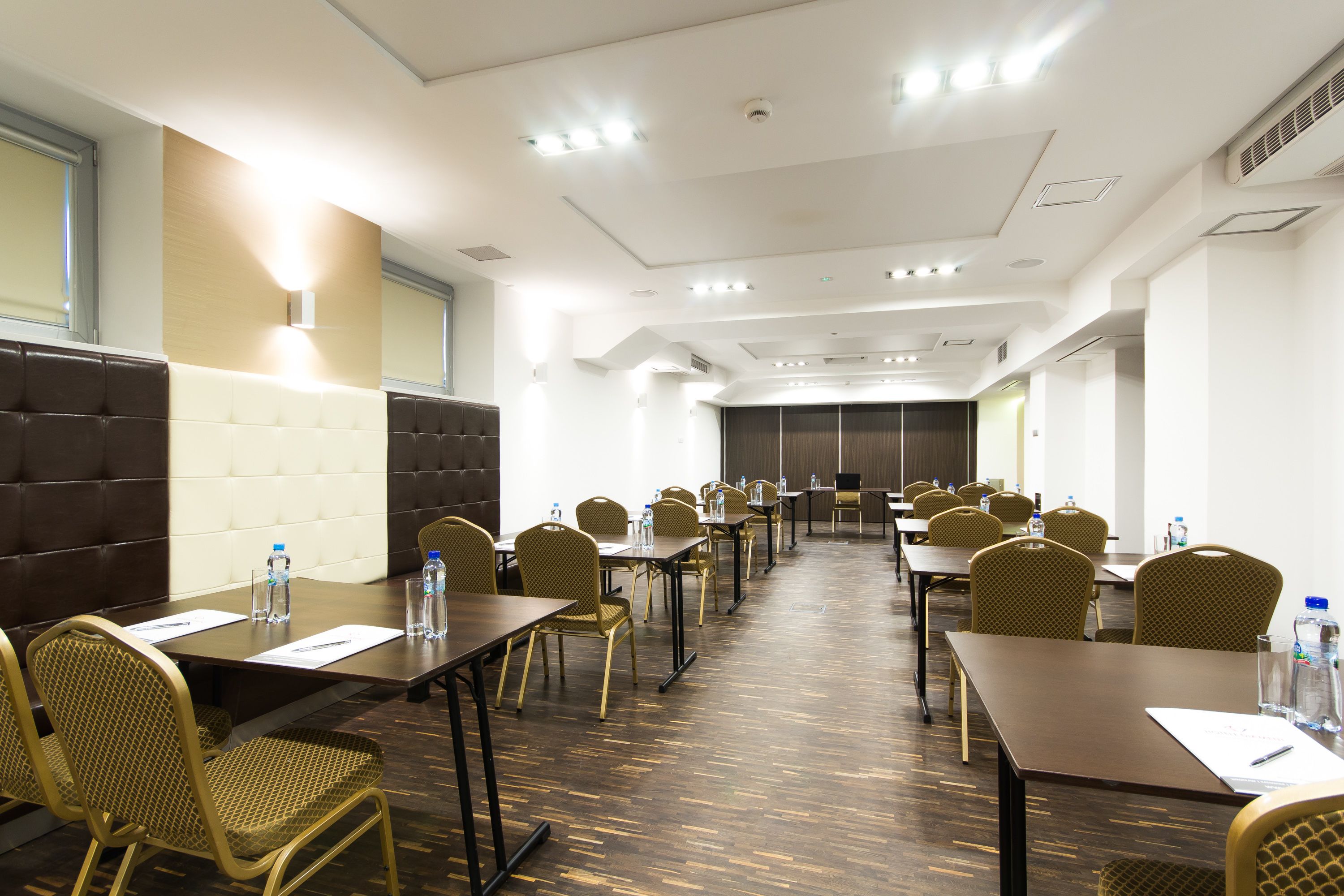 A conference room with multiple tables and chairs, equipped with water bottles and pens.