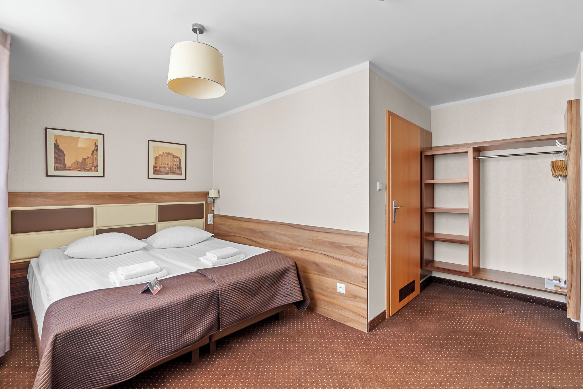 A hotel room with a bed, a wardrobe, and two framed pictures on the wall.