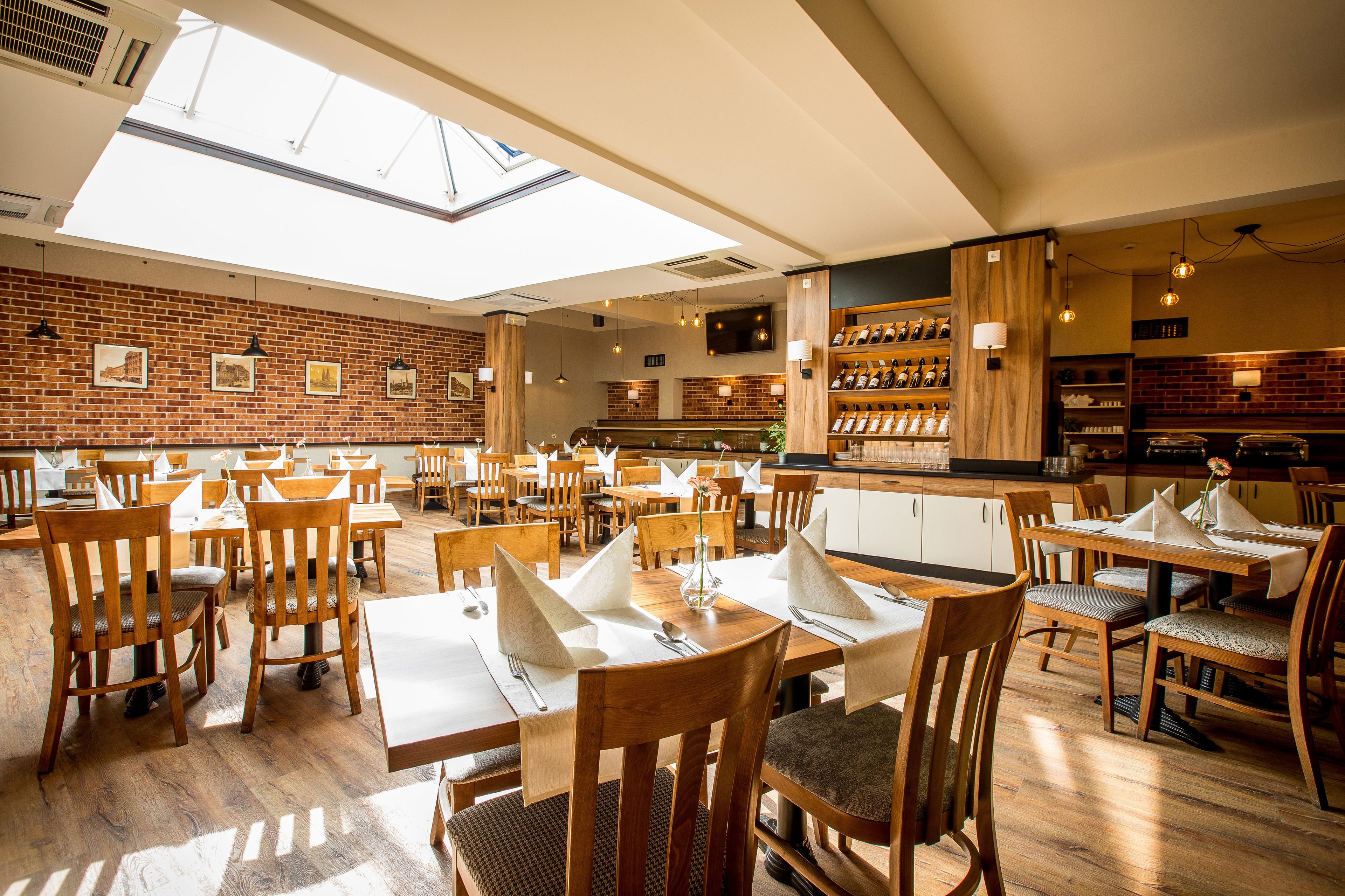 A restaurant with wooden tables and chairs, a brick wall, and a skylight.