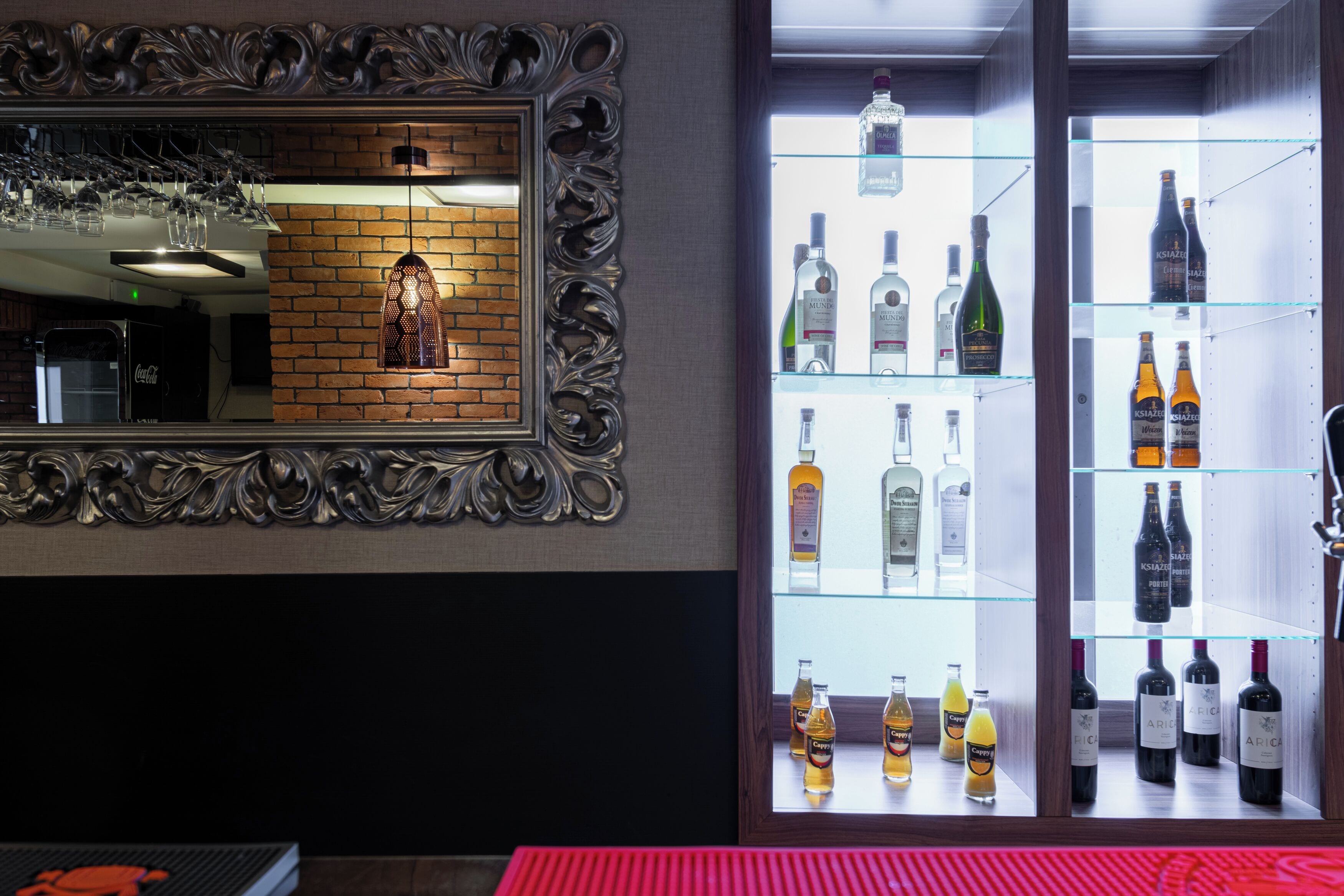 Una zona de bar con un espejo, estantes llenos de botellas de licor y vasos.