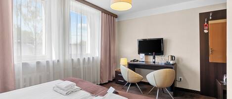 A hotel room with two beds, a desk with a TV, a chair, and a window with curtains.