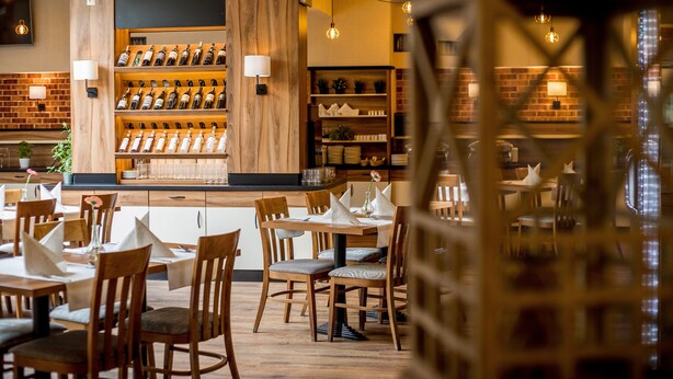 A restaurant with wooden tables and chairs, a wine rack, and a brick wall. - Hotel Diament Zabrze (Zabrze)