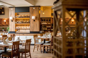 A restaurant with wooden tables and chairs, a wine rack, and a brick wall. - Hotel Diament Zabrze (Zabrze)