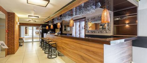 A modern bar area with a wooden counter, hanging pendant lights, and a seating area with chairs.