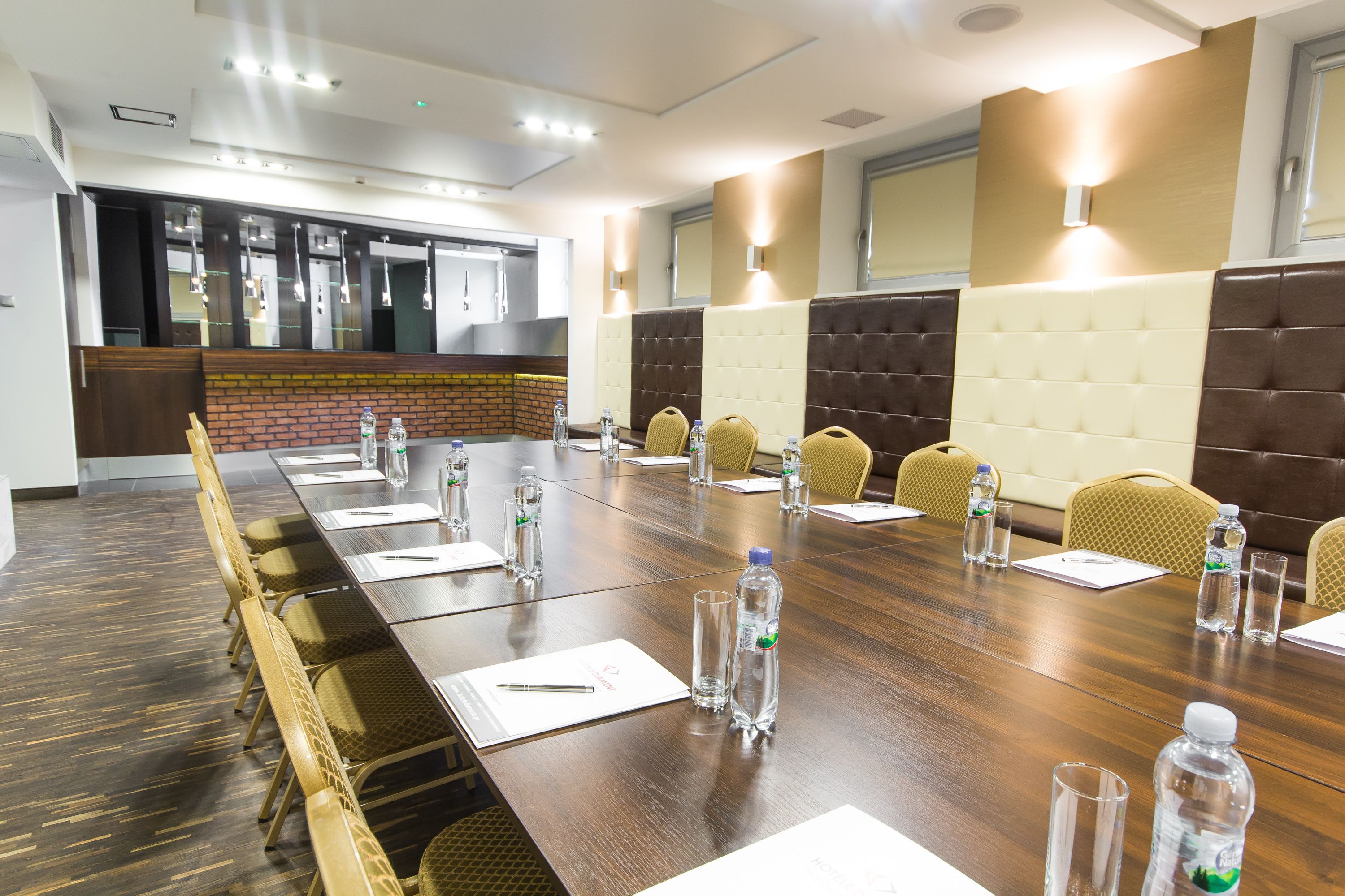 A conference room with a long table, chairs, water bottles, and a brick accent wall.