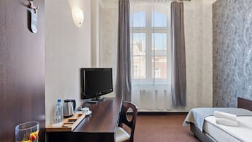 Una habitación de hotel con cama, escritorio con computadora, silla, ventana con cortinas y vista a edificios.