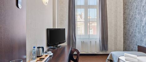 Una habitación de hotel con cama, escritorio con computadora, silla, ventana con cortinas y vista a edificios.