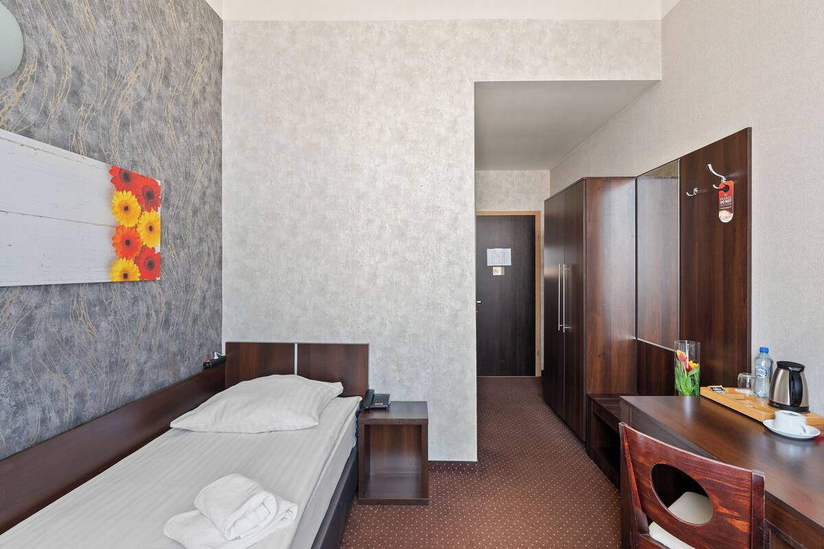 Een hotelkamer met een bed, nachtkastje, spiegel, houten bureau en kledingkast.