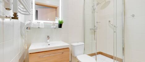 Un baño moderno con cabina de ducha de vidrio, lavamanos blanco y tocador de madera.