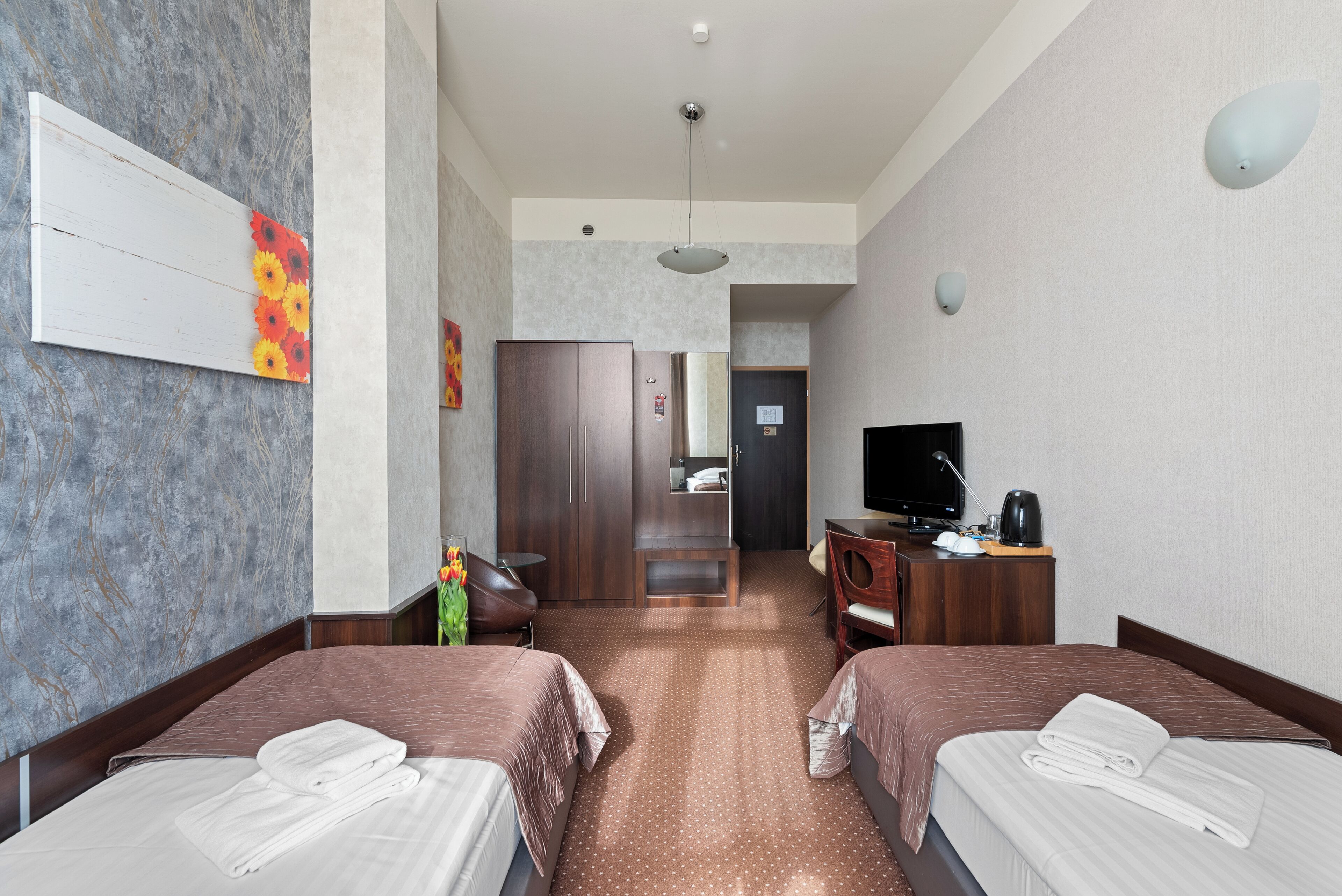 Habitación de hotel con dos camas, un escritorio con silla, televisión y baño a la vista.