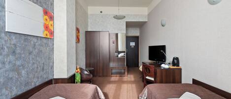 Habitación de hotel con dos camas, un escritorio con silla, televisión y baño a la vista.