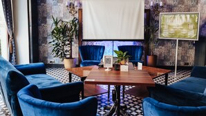 Una habitación con una mesa de madera, sillas azules, una pantalla de proyector y un papel tapiz estampado.