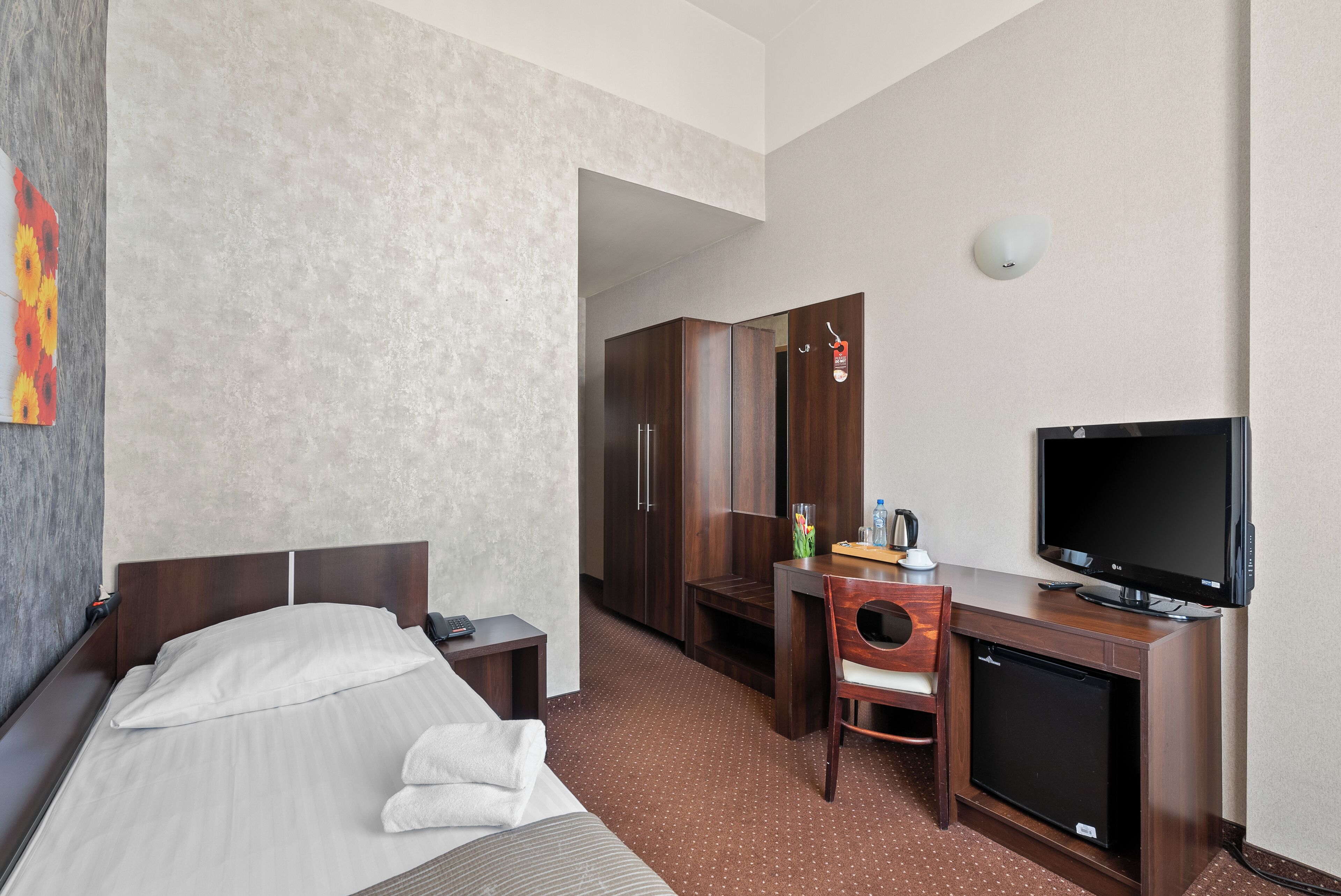 Quarto de hotel com cama, escrivaninha, cadeira, televisão e guarda-roupa.