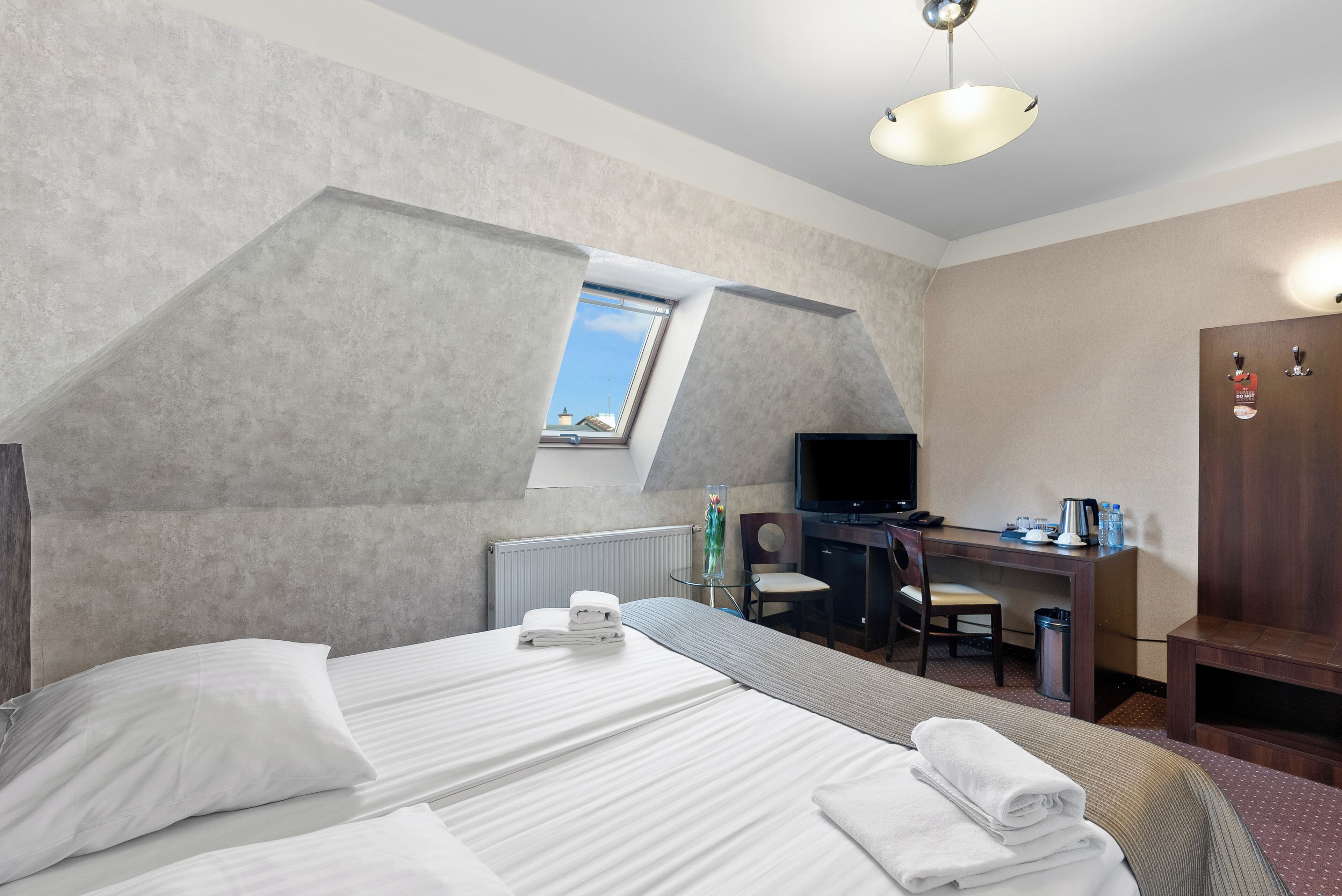 Habitación de hotel con una cama grande, un escritorio con silla, televisión y una ventana pequeña.