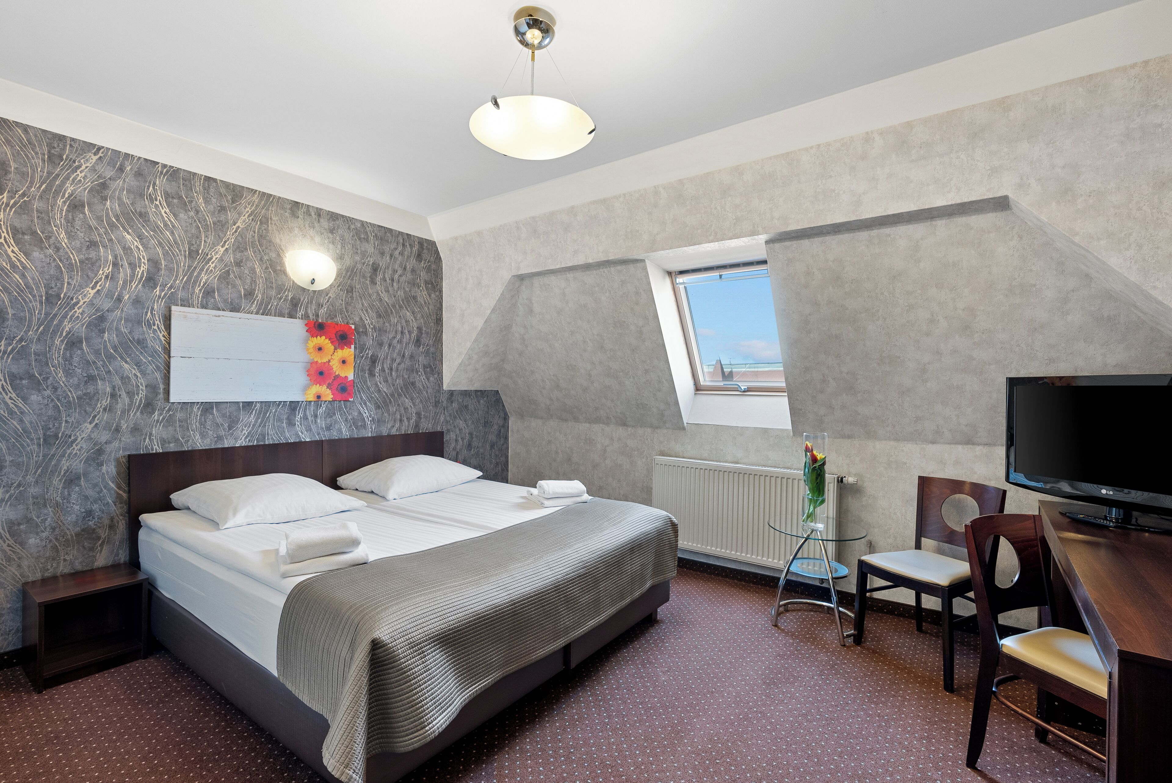Una habitación de hotel moderna con una cama grande, un escritorio con una silla, un televisor y una ventana con vistas.