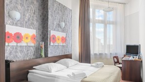 Habitación de hotel con cama, mesitas de noche, escritorio con silla, televisor y obras de arte en las paredes.