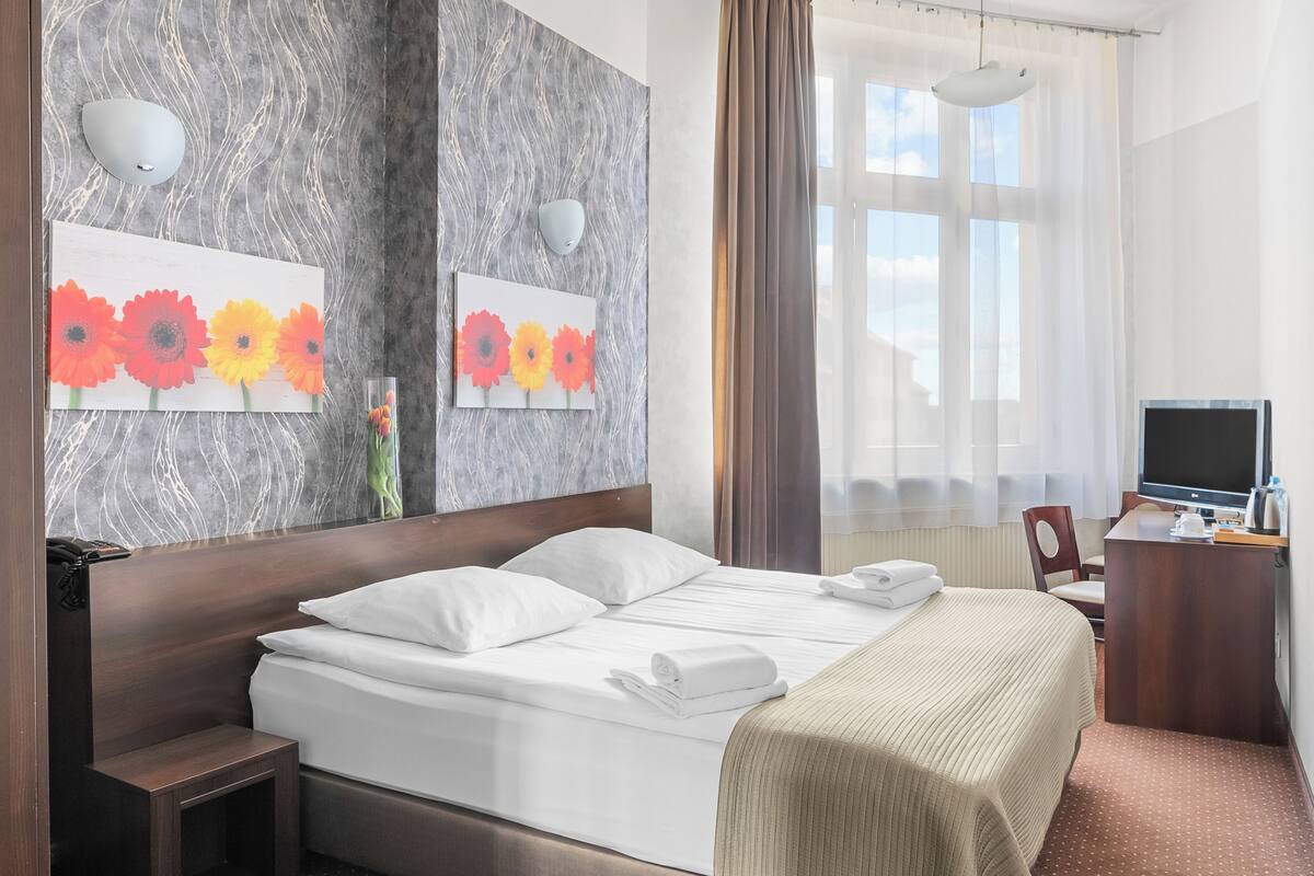 Hotelkamer met een bed, nachtkastjes, een bureau met stoel, een televisie en kunst aan de muren.