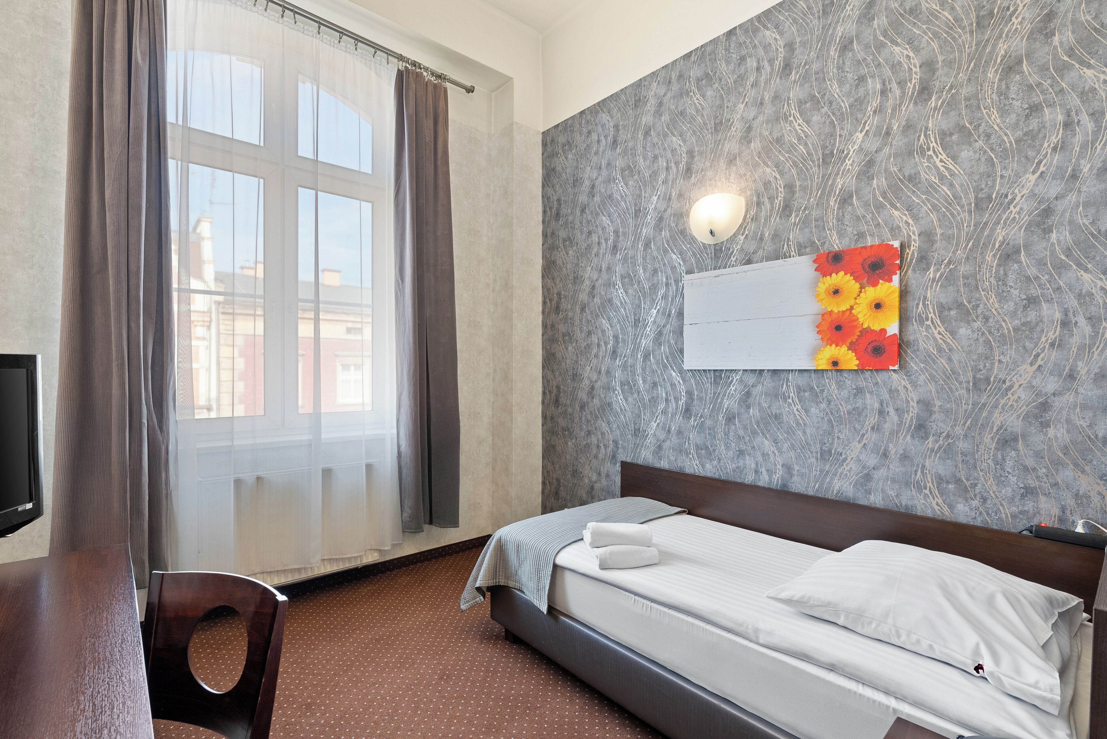 Una habitación de hotel con cama, televisión, escritorio y ventana con cortinas.