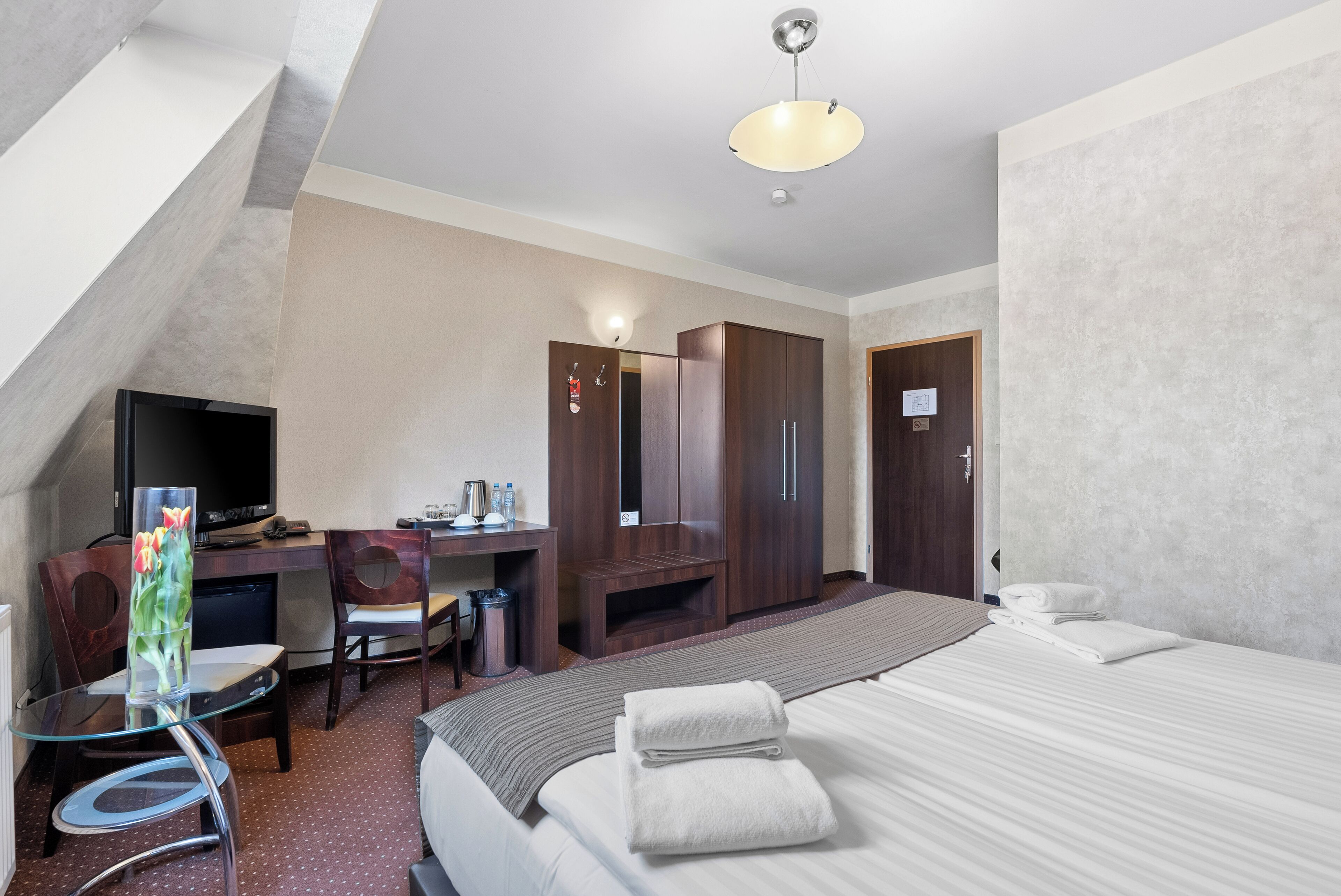Una camera d'albergo con un letto, una scrivania, una sedia, una televisione e un armadio.