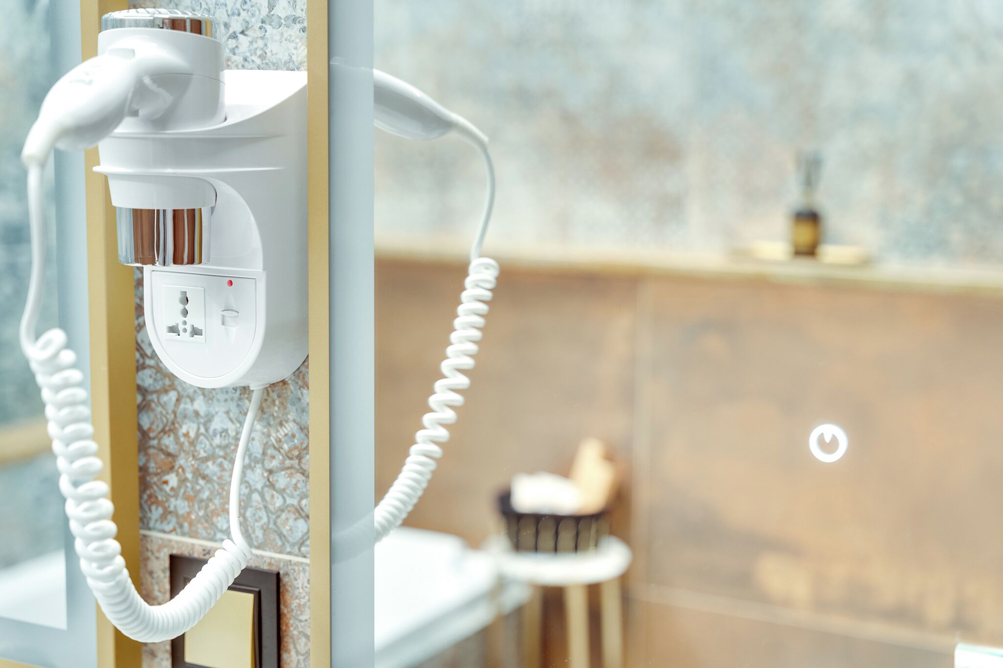 A hair dryer and phone charger mounted on a wall with a marble backsplash and a small countertop with a candle.