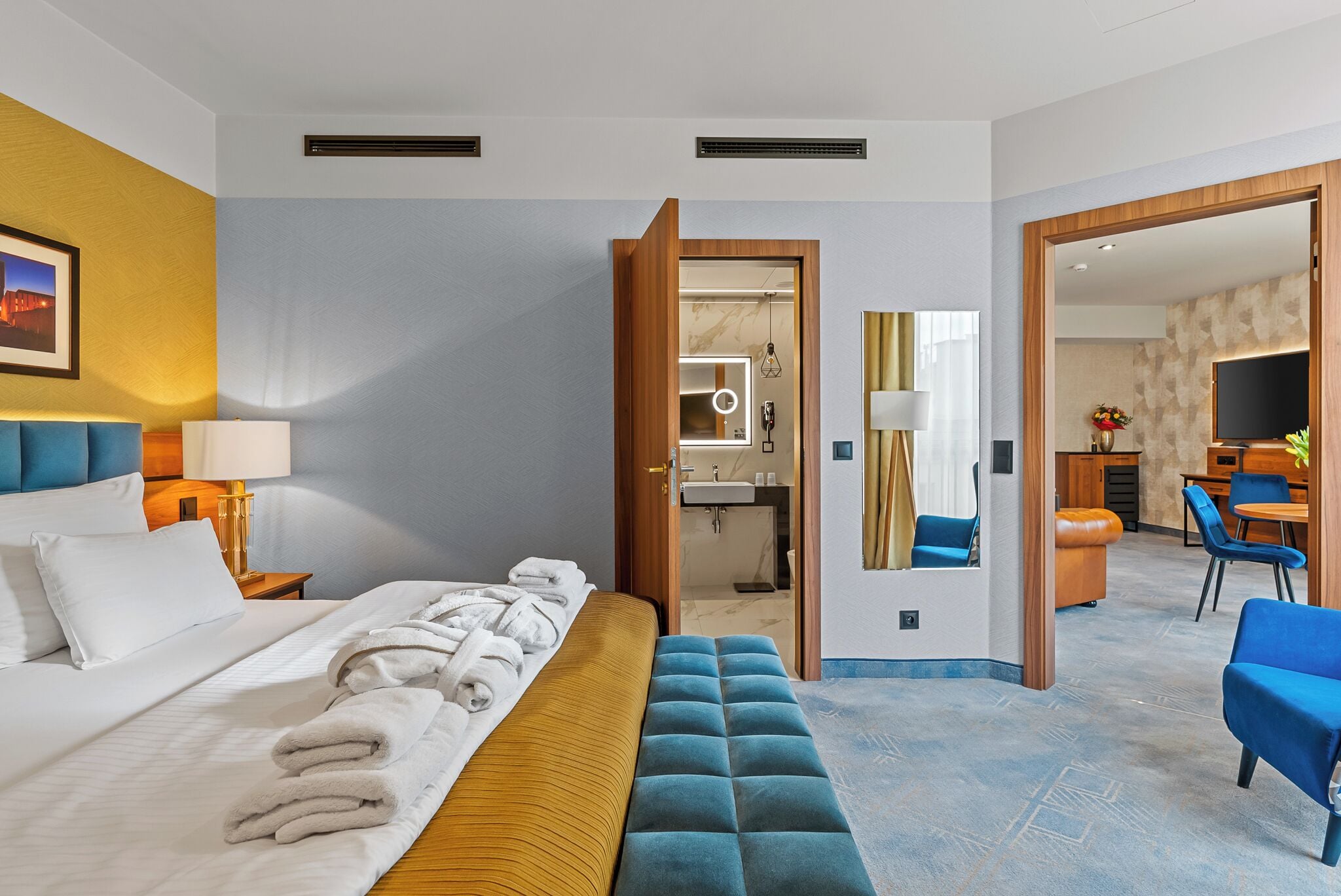 A hotel room with a bed, bedside table, lamp, and a bathroom visible through an open door.
