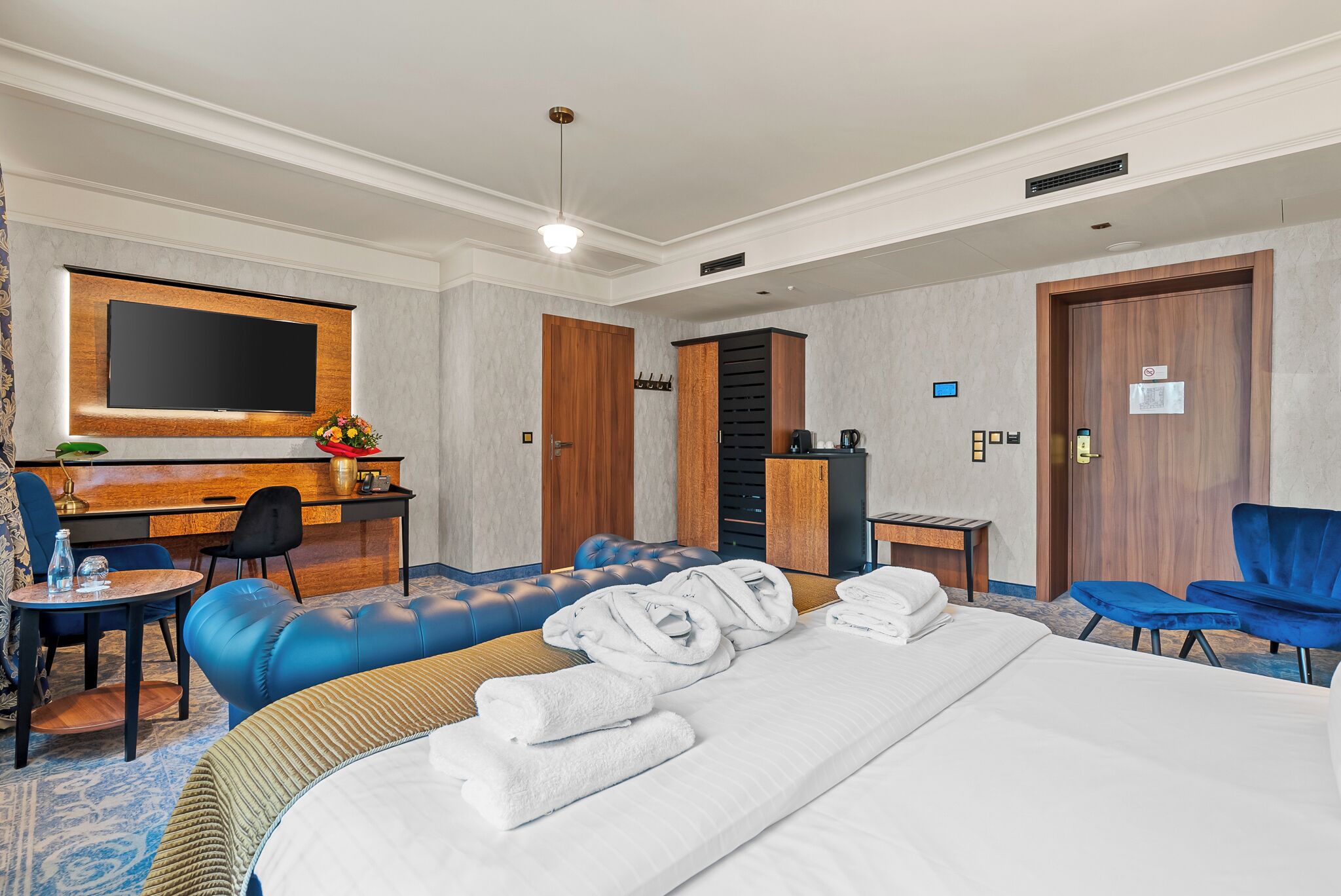 A hotel room with a bed, a desk, a TV, a seating area, and a bathroom.
