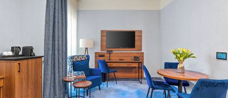 Hotelkamer met een houten bureau, een flatscreen televisie, een bank, een salontafel en een eettafel met stoelen.