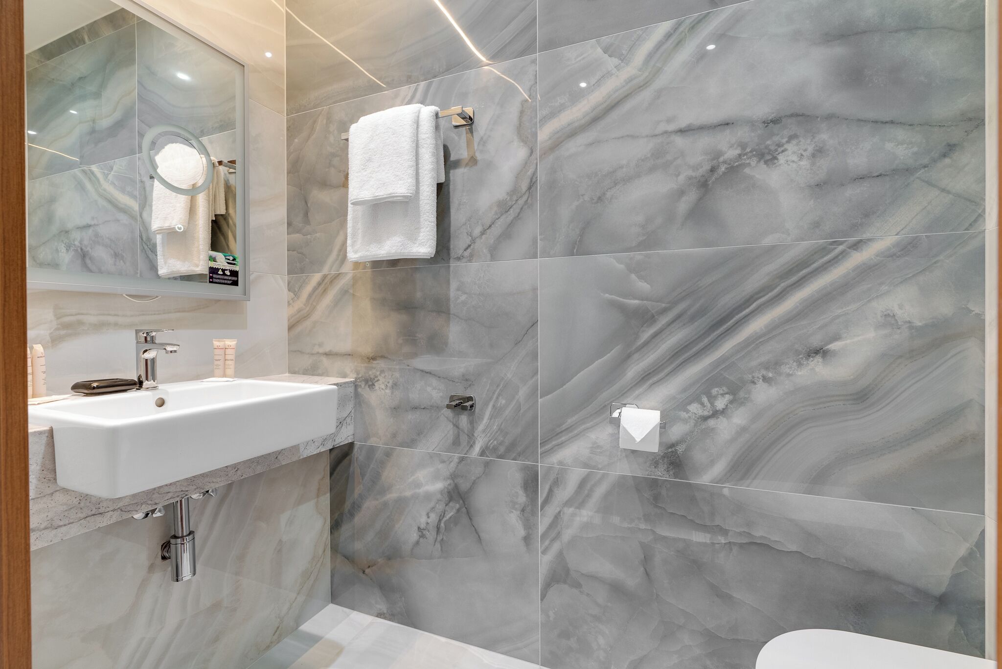 Ein Badezimmer mit Marmorwand, Waschbecken, Spiegel und Handtuchhalter.