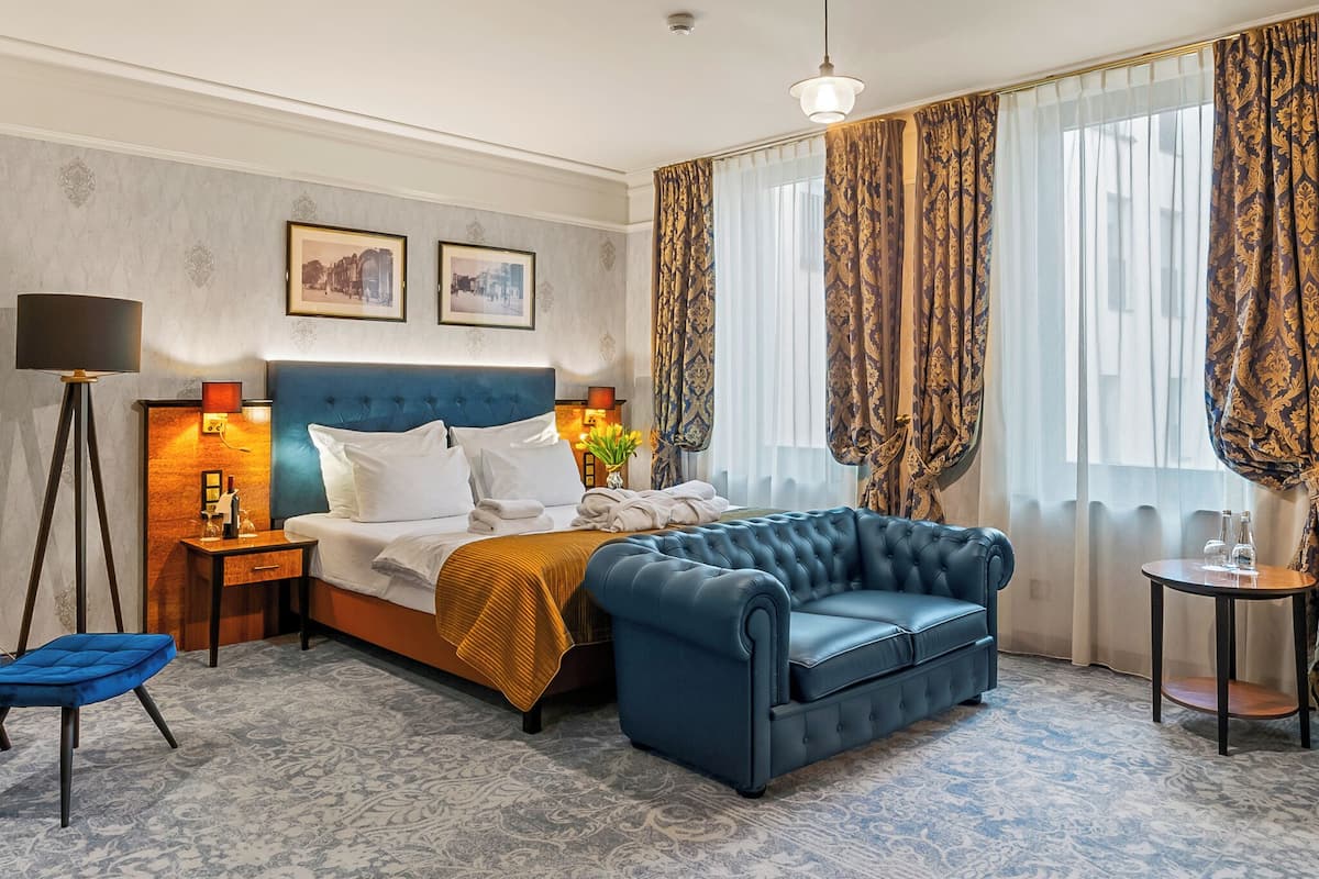 A hotel room with a large bed, a blue sofa, a small table, and a lamp.