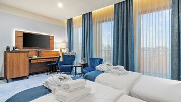 Habitación de hotel con cama, escritorio, silla, televisor y ventana con cortinas.