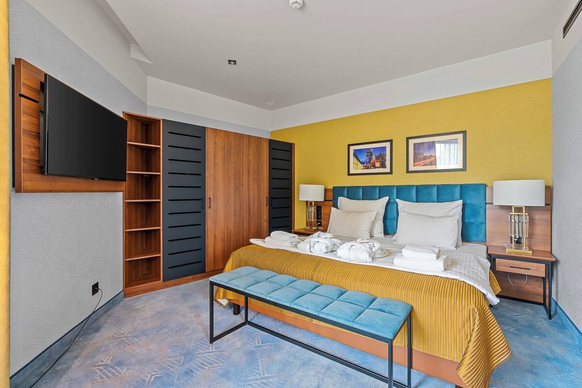 A modern hotel room with a bed, a bench, a TV, and a wardrobe.