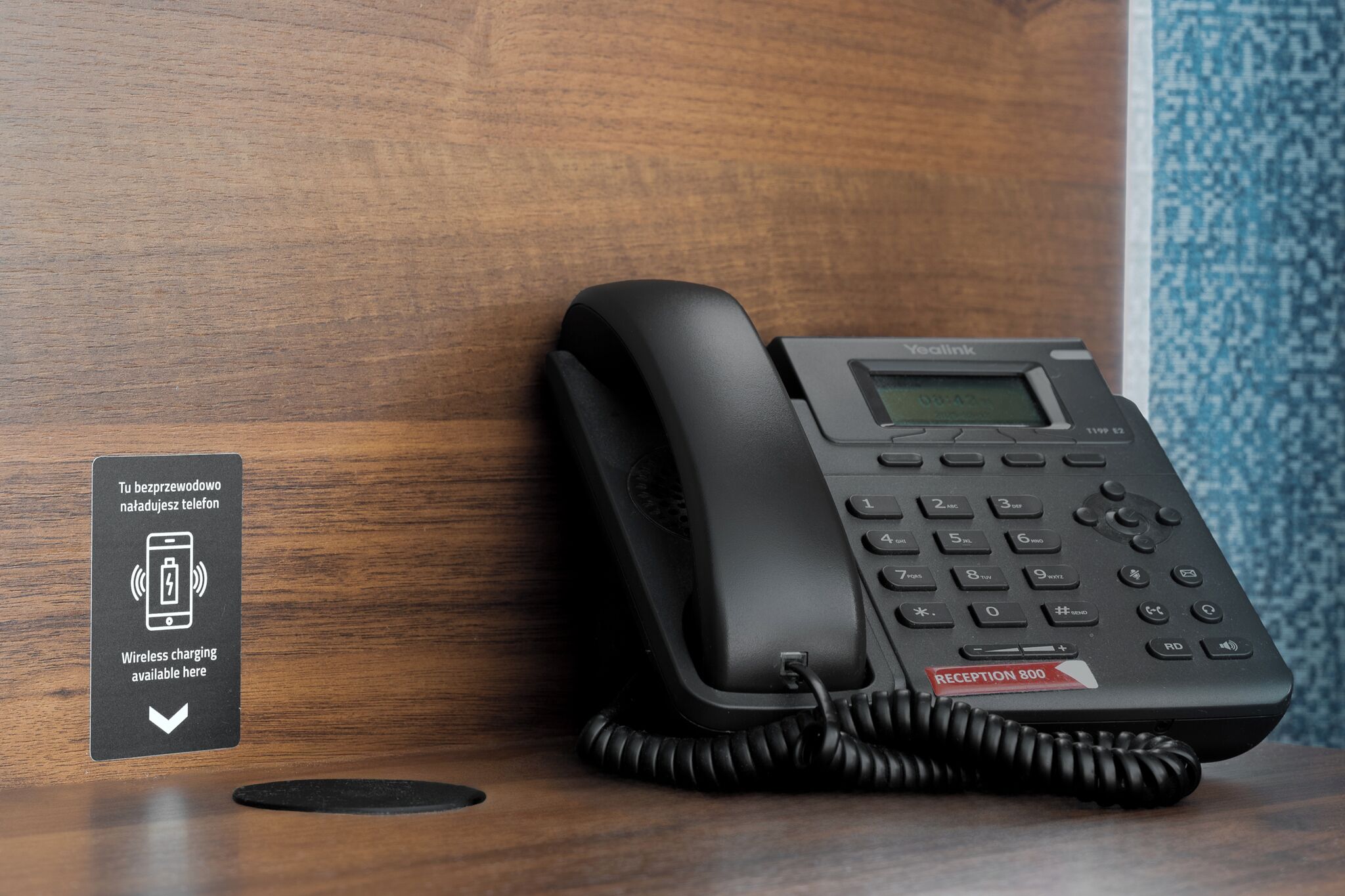 A black hotel reception phone with a digital display, a sign indicating wireless charging, and a reception label.