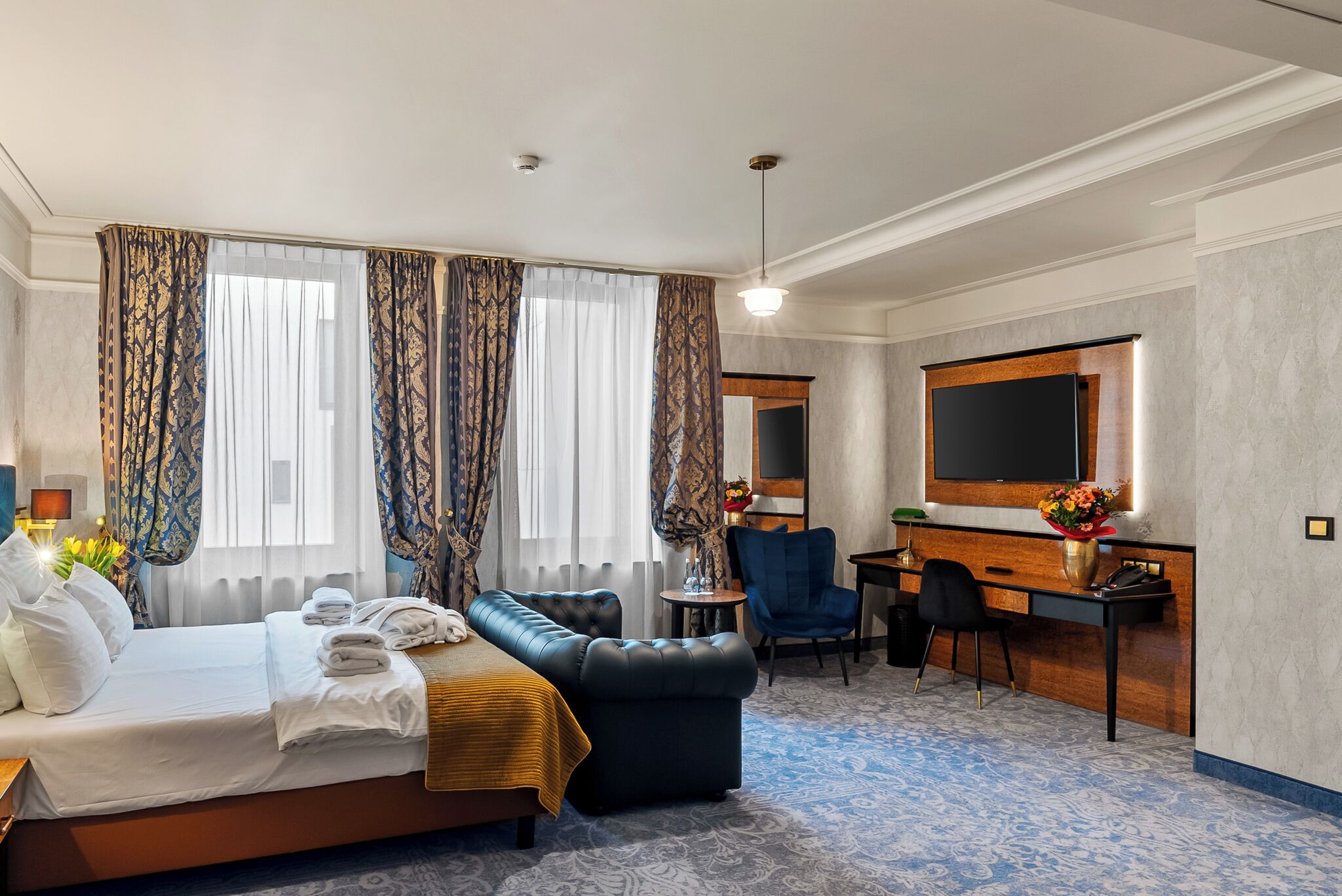 A hotel room with a bed, a desk, a chair, a television, and a large window with curtains.