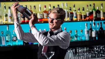 Un barman en train de servir une boisson dans un bar, avec une variété de bouteilles en arrière-plan.
