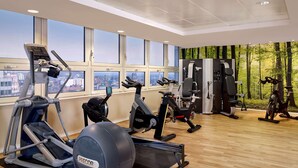 Un gimnasio con diferentes máquinas de ejercicio, amplias ventanas y vistas a la ciudad.