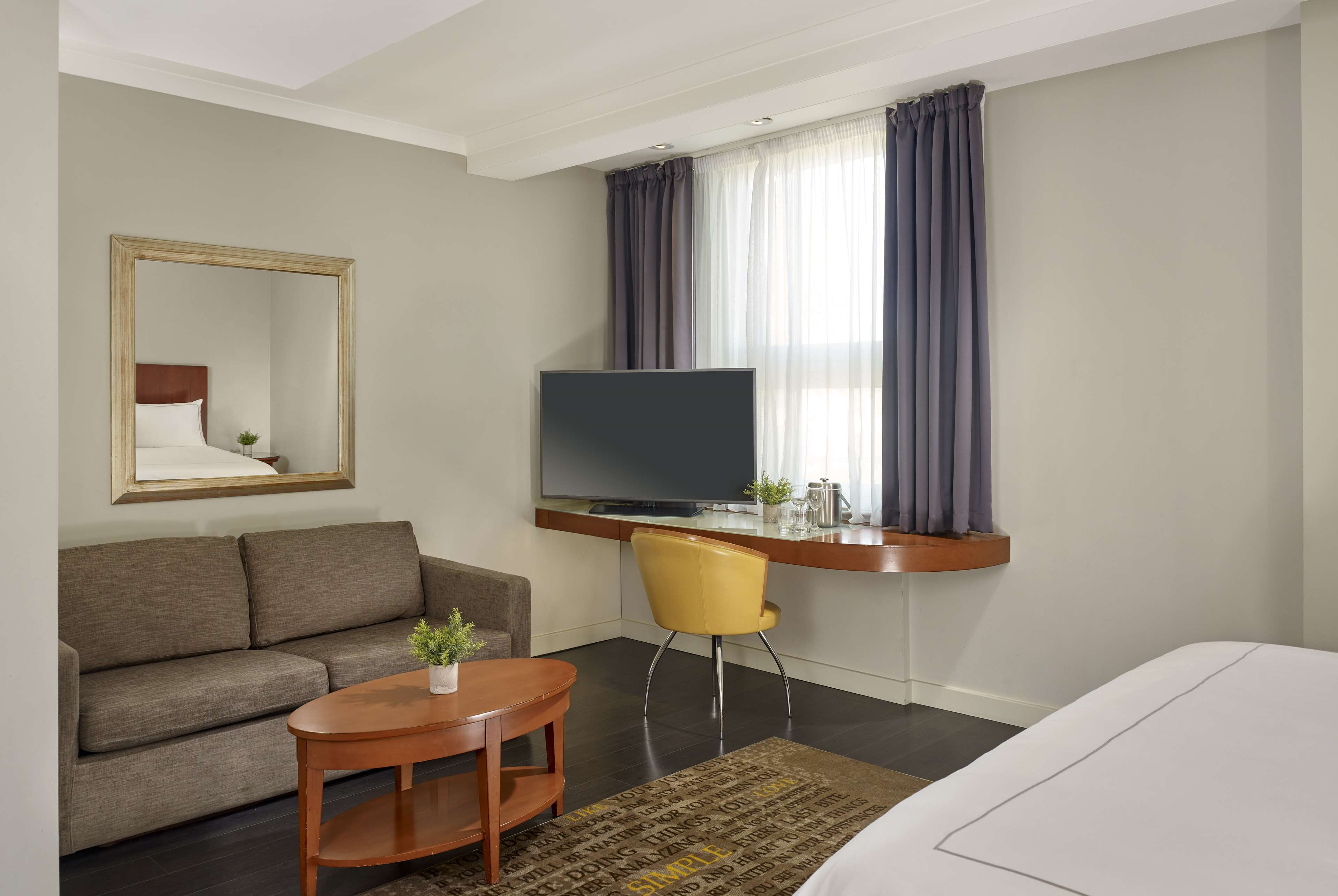 Habitación de hotel con sofá, escritorio y silla, televisor, cama y ventana con cortinas.