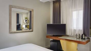 Quarto de hotel com uma cama, escrivaninha com computador, televisão, espelho e janela com cortinas.