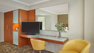 Habitación de hotel con armario de madera, televisor de pantalla plana, refrigerador pequeño, sillón amarillo y alfombra estampada.