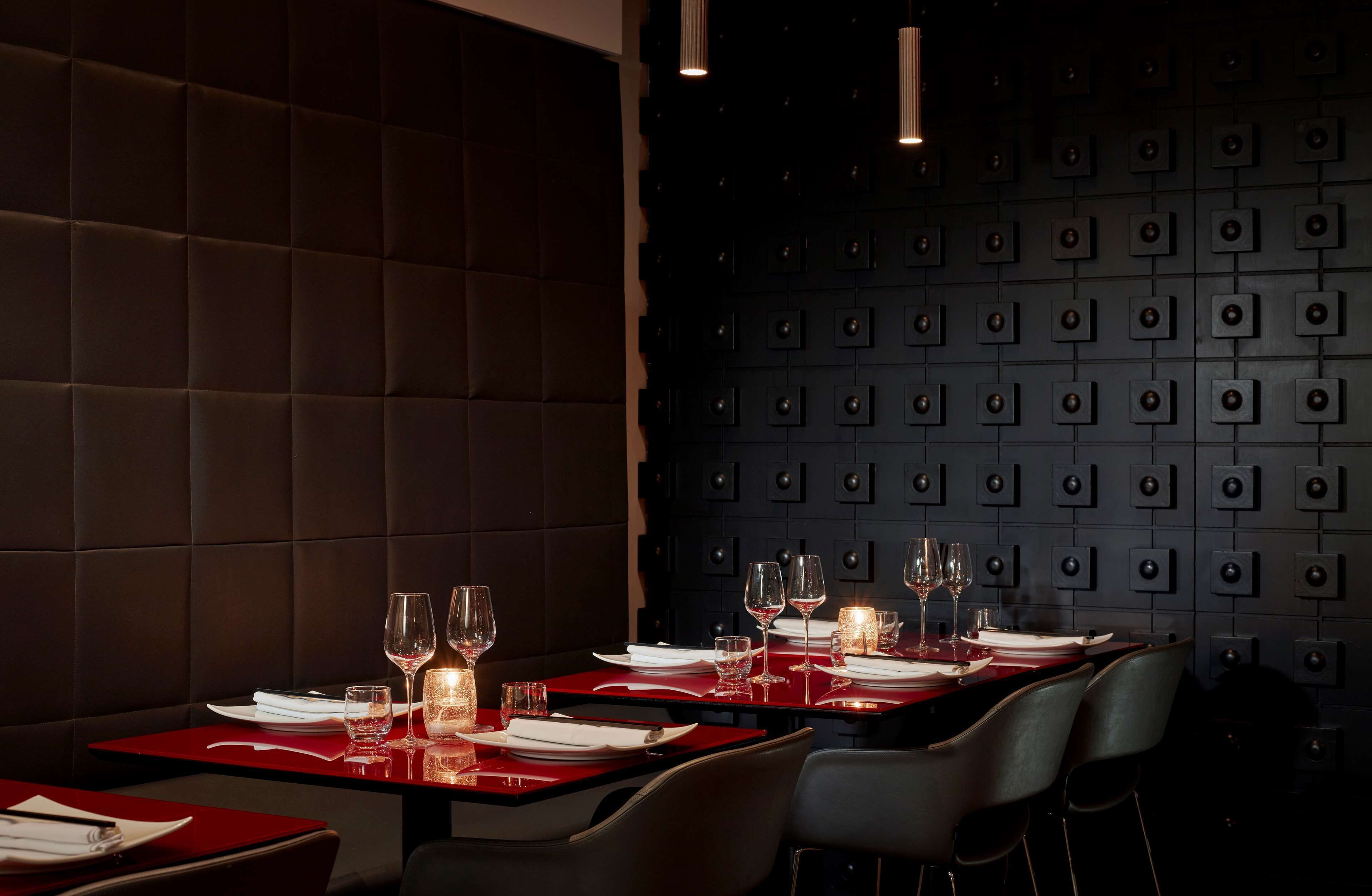 Een restaurantinterieur met rode tafels, witte servetten en kaarsen.