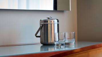 A stainless steel coffee pot and two glasses on a reflective surface.