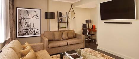 A living room with a sofa, a coffee table, a bookshelf, and a TV mounted on the wall.