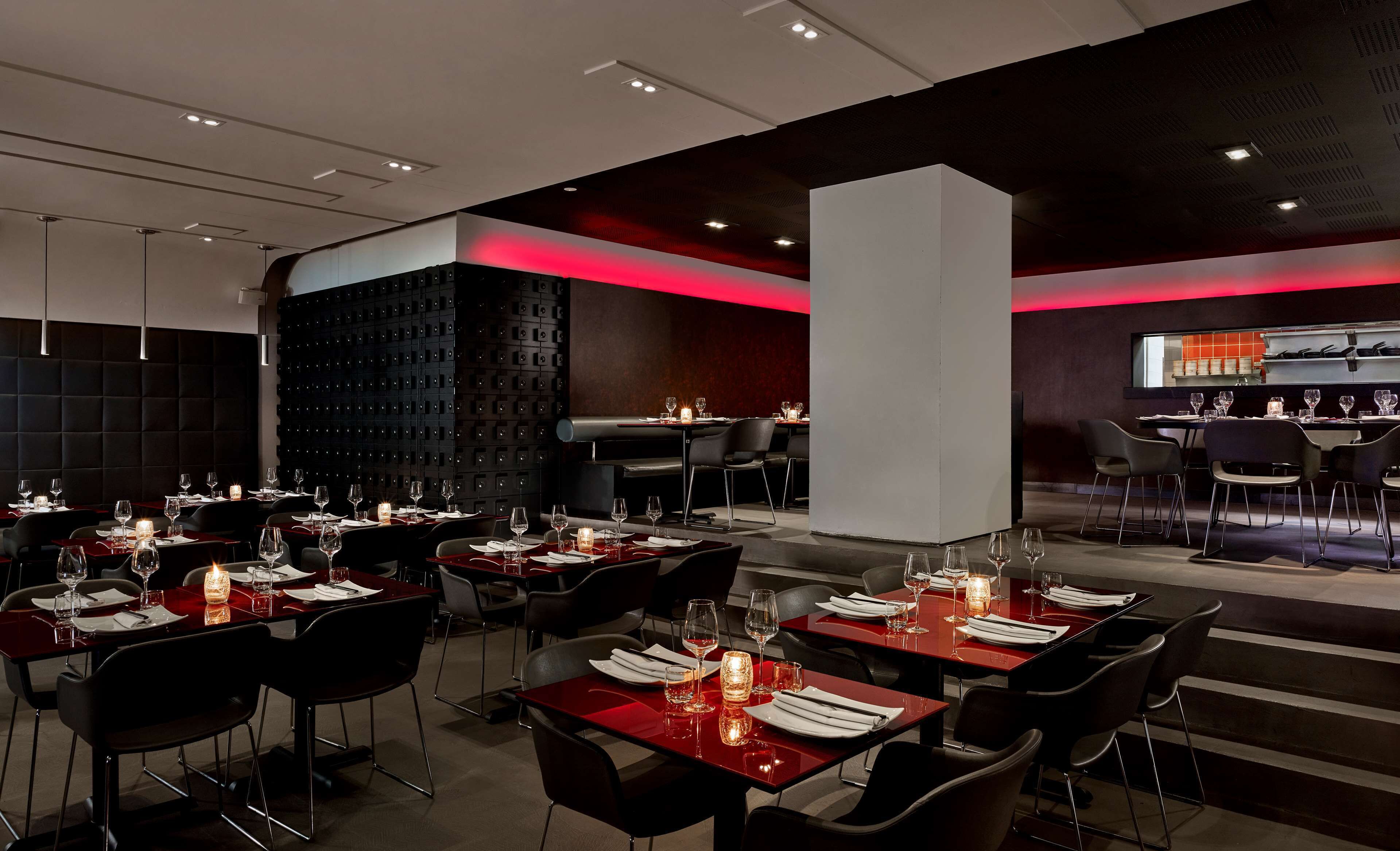 A modern restaurant with red tables and black chairs, featuring a unique black wall with embedded lights.