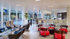 Un moderno vestíbulo de hotel con diferentes opciones de asientos, incluyendo sillas y sofás, y grandes ventanales que ofrecen vistas a la calle.
